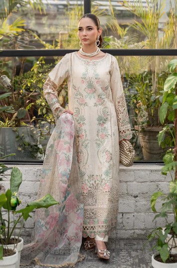 Elegant embroidered beige lawn dress with floral patterns, lace sleeves, and a sheer dupatta, styled with pearl jewelry in a lush green setting.